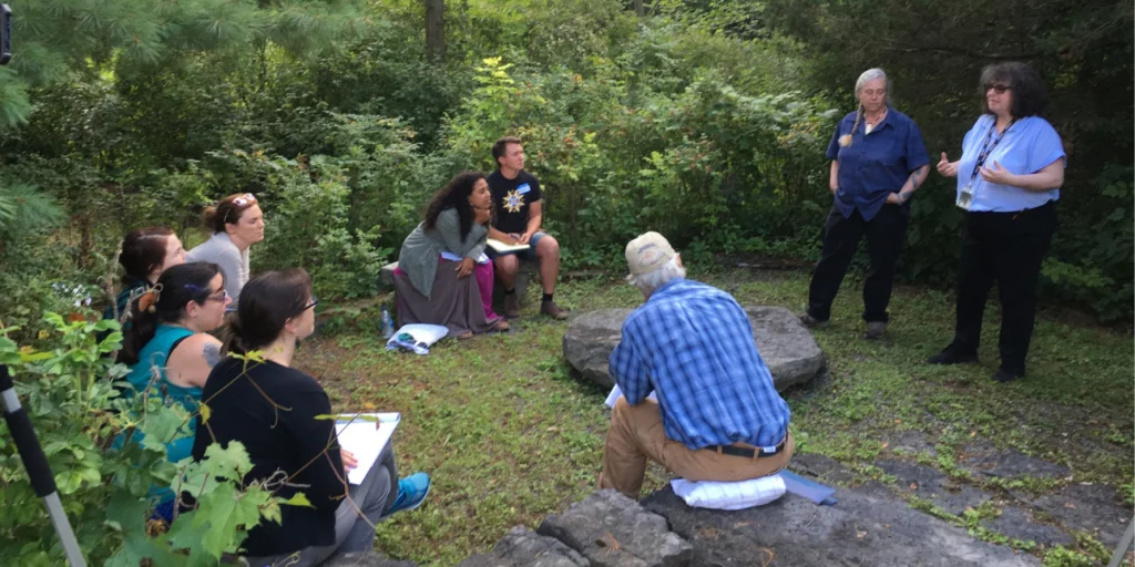 A group of teachers sitting in an outdoor garden classroom listening to their instructors.