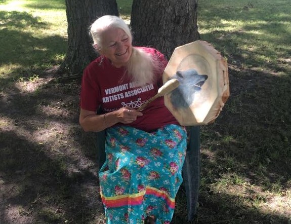 A woman hitting a hand drum with a wolf painted on it.